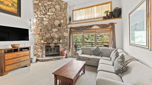 A living room with a stone fireplace, a sofa, a coffee table, and a flat-screen TV. - Private Balcony + Grill, Walk to Mountain House Base Area, Shared Hot Tub (Keystone)