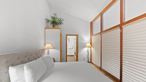 A neatly arranged hotel room with a large bed, two bedside lamps, a potted plant, and a view through a window with blinds. - Private Balcony + Grill, Walk to Mountain House Base Area, Shared Hot Tub (Keystone)