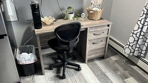 A compact office space with a wooden desk, a black office chair, a coffee maker, a potted plant, and a basket with magazines. - 1 bedroom 1 bath private entrance (Bay Shore)