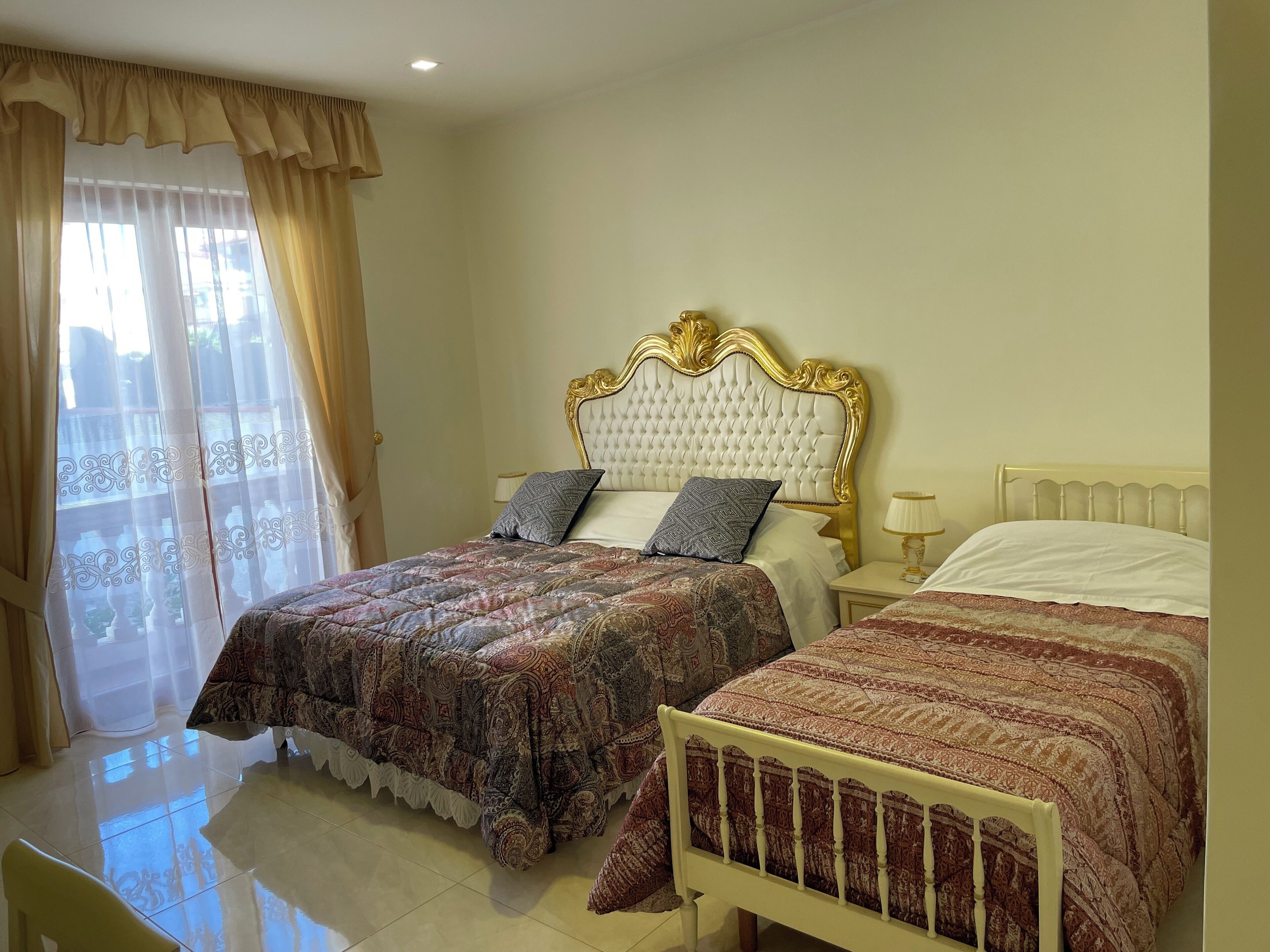 Habitación de hotel con dos camas, un ventanal con cortinas, una araña y vistas a un balcón.