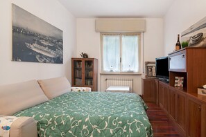 Un dormitorio con cama, televisión, armario, ventana y un cuadro en la pared.
