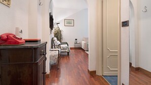 Un couloir avec un plancher en bois, un téléphone rouge, un meuble, une chaise, une petite table et une porte.