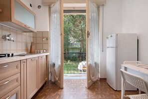 Una cocina con armarios de madera, una encimera, un refrigerador y vista a un jardín a través de una puerta abierta.