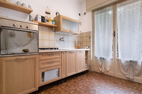 A kitchen with wooden cabinets, a stove, and a window with curtains. - Apartment "Casa Rizzo" with Garden & Wi-Fi (Rapallo)