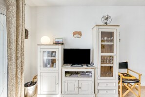 Een woonkamer met een televisie, kasten, een fauteuil en een decoratief wandobject.