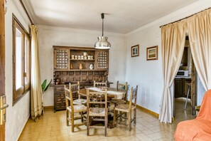 A dining area with a wooden table and chairs, a cabinet with kitchenware, and a hanging light fixture. - Holiday Home "Casa Saguer" with Terrace, Garden & Pool (L'Escala)