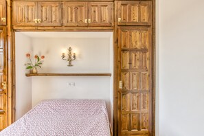 A room with a bed, wooden cabinets, a shelf with flowers, and a wall-mounted light fixture. - Holiday Home "Casa Saguer" with Terrace, Garden & Pool (L'Escala)