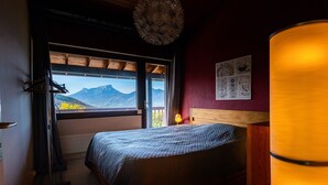 Une chambre à coucher avec un lit, une fenêtre donnant sur les montagnes, une lampe fixée au mur et un luminaire au plafond.