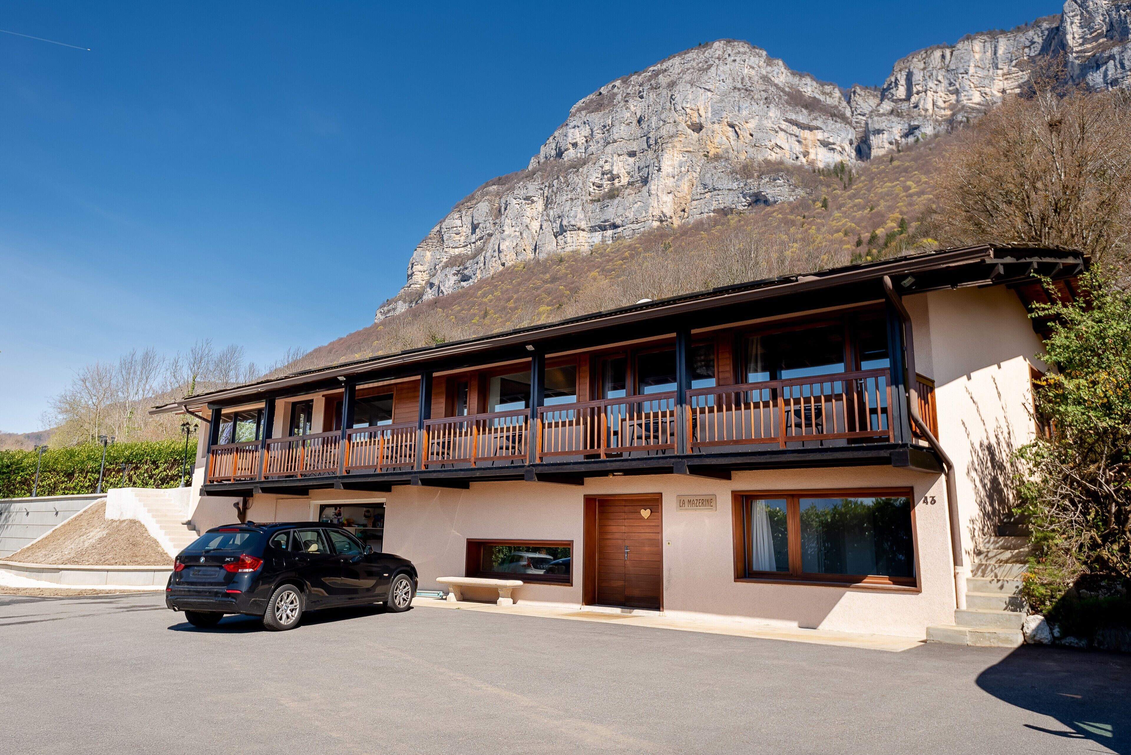 Een gebouw met twee verdiepingen met een balkon, een auto voor en een berg op de achtergrond.