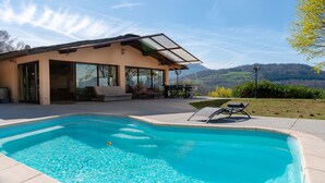 Une maison moderne dotée d’une piscine, de grandes fenêtres et offrant une vue sur les collines.