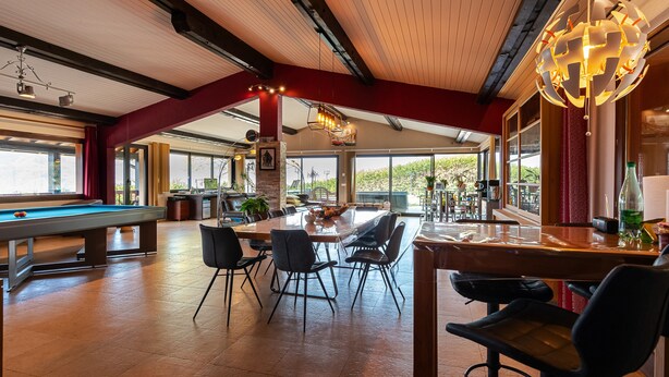 Un espace intérieur vaste et lumineux, comprenant une table de billard, des chaises de salle à manger, un coin bar et de grandes fenêtres offrant une vue panoramique.