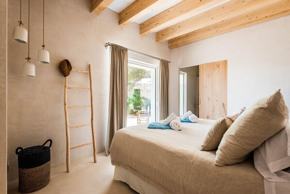 A bedroom with a bed, wooden beams, a ladder, a window, and a woven basket.