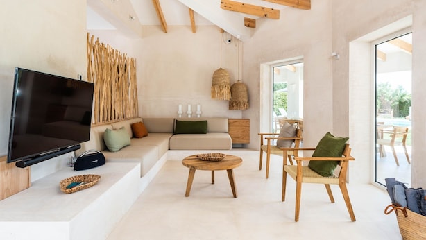 Un salon moderne doté d’un téléviseur à écran plat, de meubles en bois, d’un canapé avec des coussins et d’une grande fenêtre.