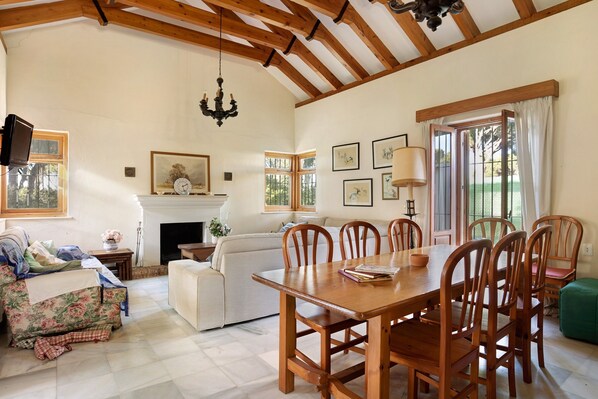 A spacious living room with a fireplace, a dining area with wooden chairs, and a large window with curtains.