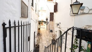 Un estrecho callejón con una escalera que conduce a la entrada de un edificio, rodeado de paredes blancas y barandillas de metal negro.