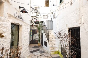 Une ruelle étroite avec un bâtiment blanc portant l’inscription « Cantina », un escalier et une petite boutique dont la vitrine est visible.