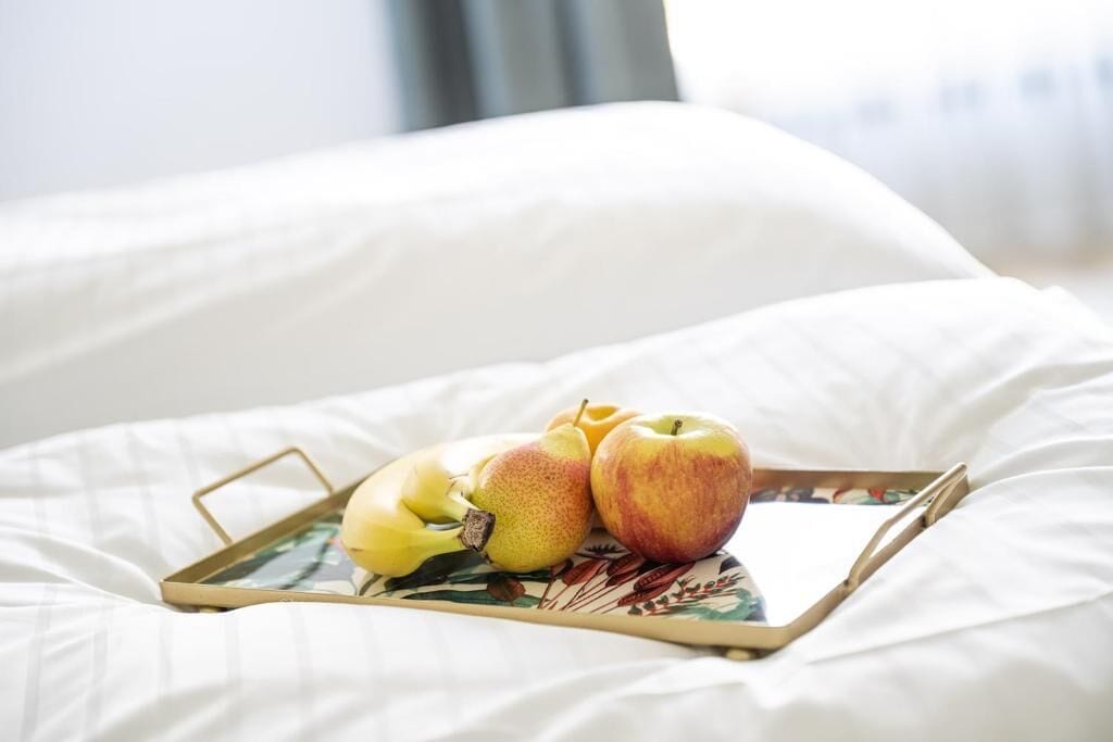 A tray with apples and pears on a bed with white bedding.