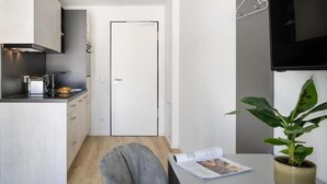 Una cocina compacta con electrodomésticos modernos, un comedor con una silla gris y una planta en maceta.