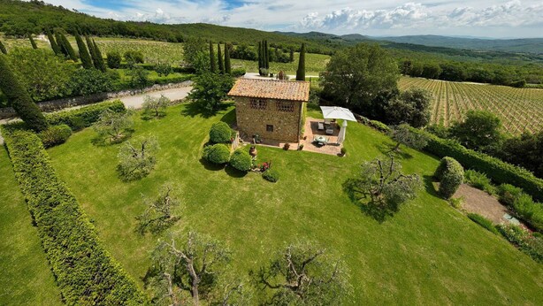 Una casa de pedra amb teulada d'àmita envoltat de jardins ben cuidats i vinyes.