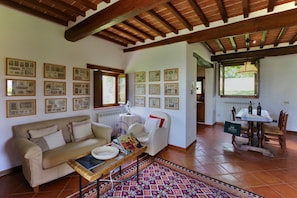 A cozy living room with a sofa, a coffee table, and a patterned rug. There are framed pictures on the walls and a window with a view of the outdoors.