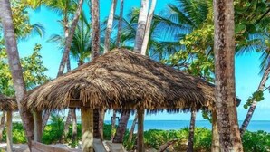 A beach hut with a thatched roof, surrounded by palm trees and a sandy beach.