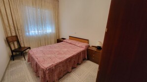 Un dormitorio con una cama individual, una silla, una mesita de noche y una lámpara.