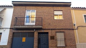 Un edificio de dos plantas con fachada de ladrillo, balcón, puerta de garaje y puerta principal.