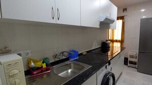 Cocina compacta con armarios blancos, pileta de acero inoxidable, lavadora y refrigerador.