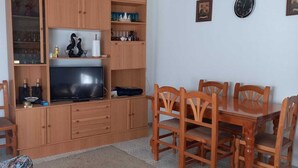Un espacio habitable compacto con televisor, muebles de madera y estantes con diversos objetos.