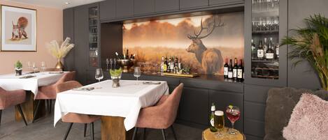 A modern bar area with a large mural of a deer, wine bottles, and glasses on shelves.