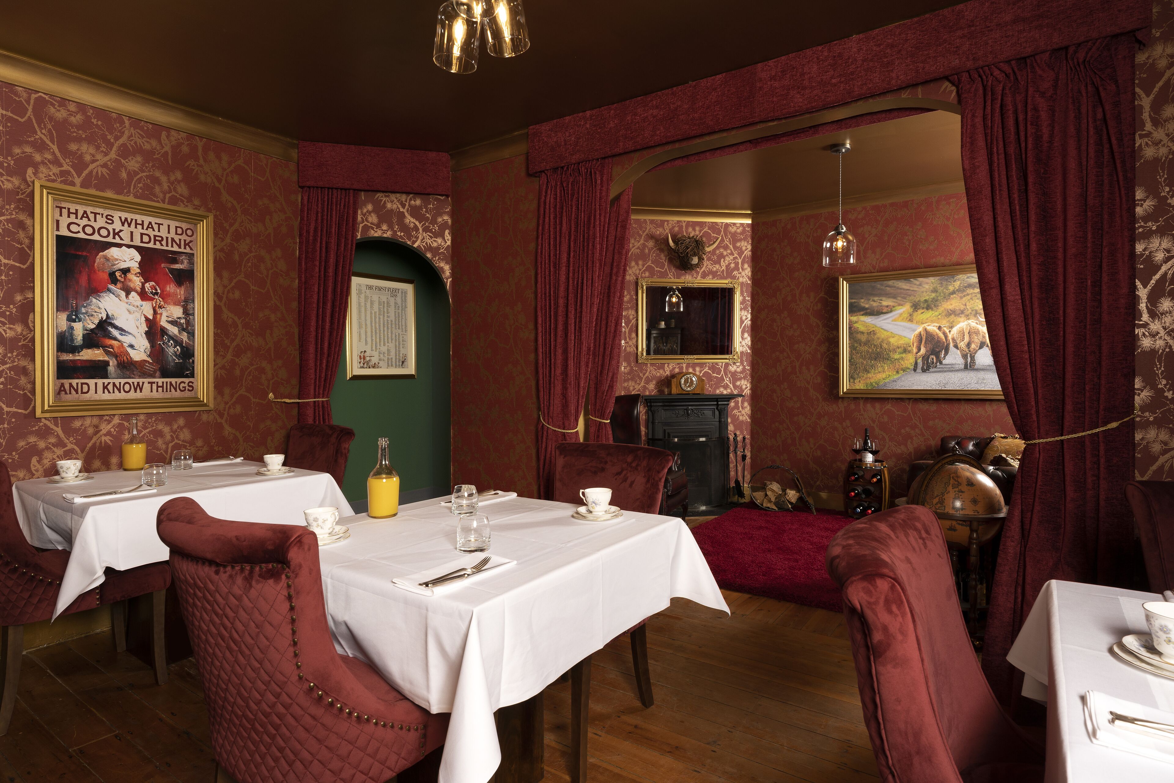A dining area with tables set for two, red velvet chairs, and a vintage decor.