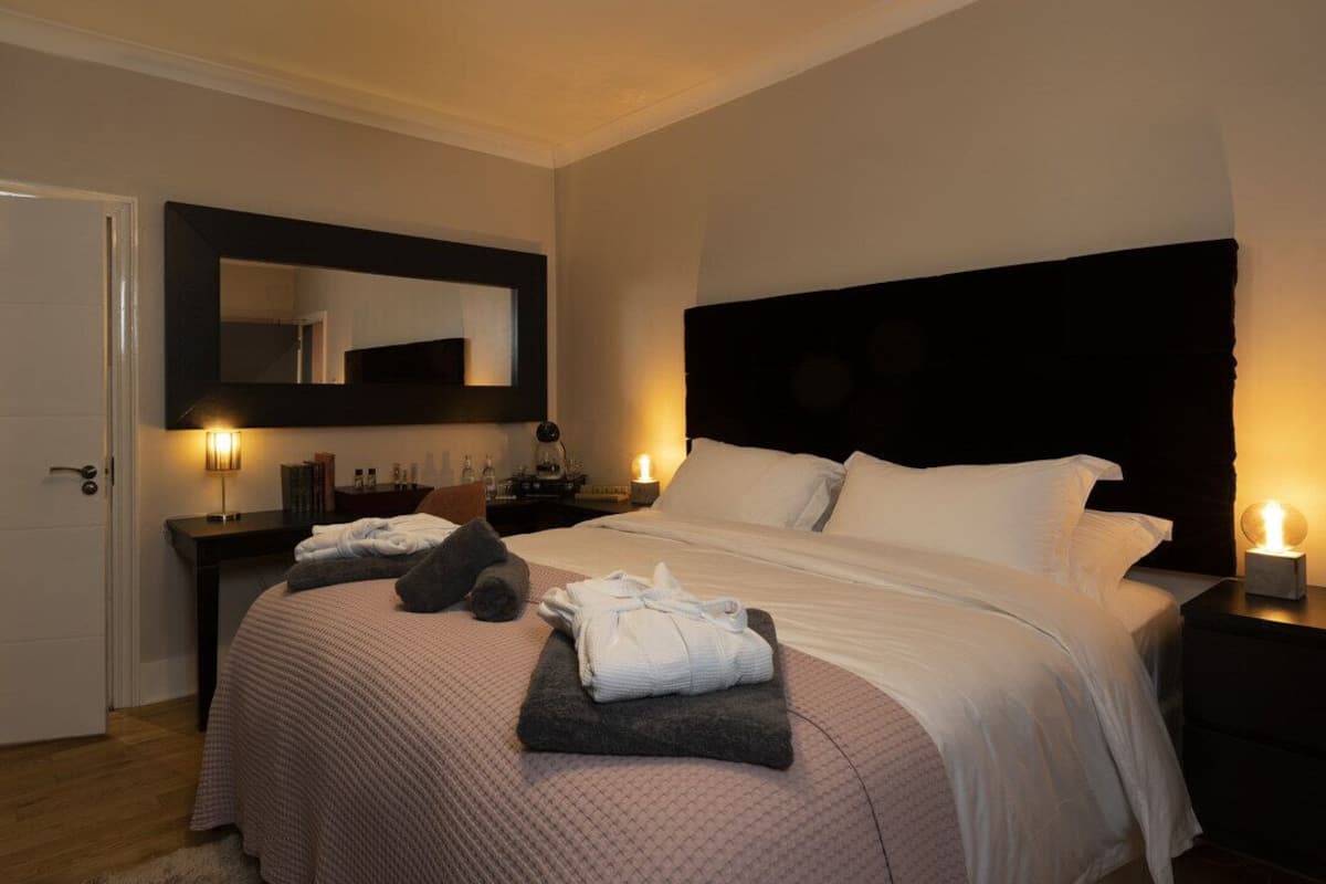 A neatly made bed with a headboard, a bedside table with a lamp, and a mirror on the wall.