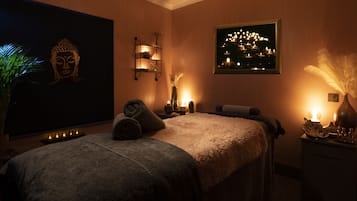 A spa room with a large Buddha painting, a bed with towels, a wall-mounted light, and a framed picture of a cityscape.