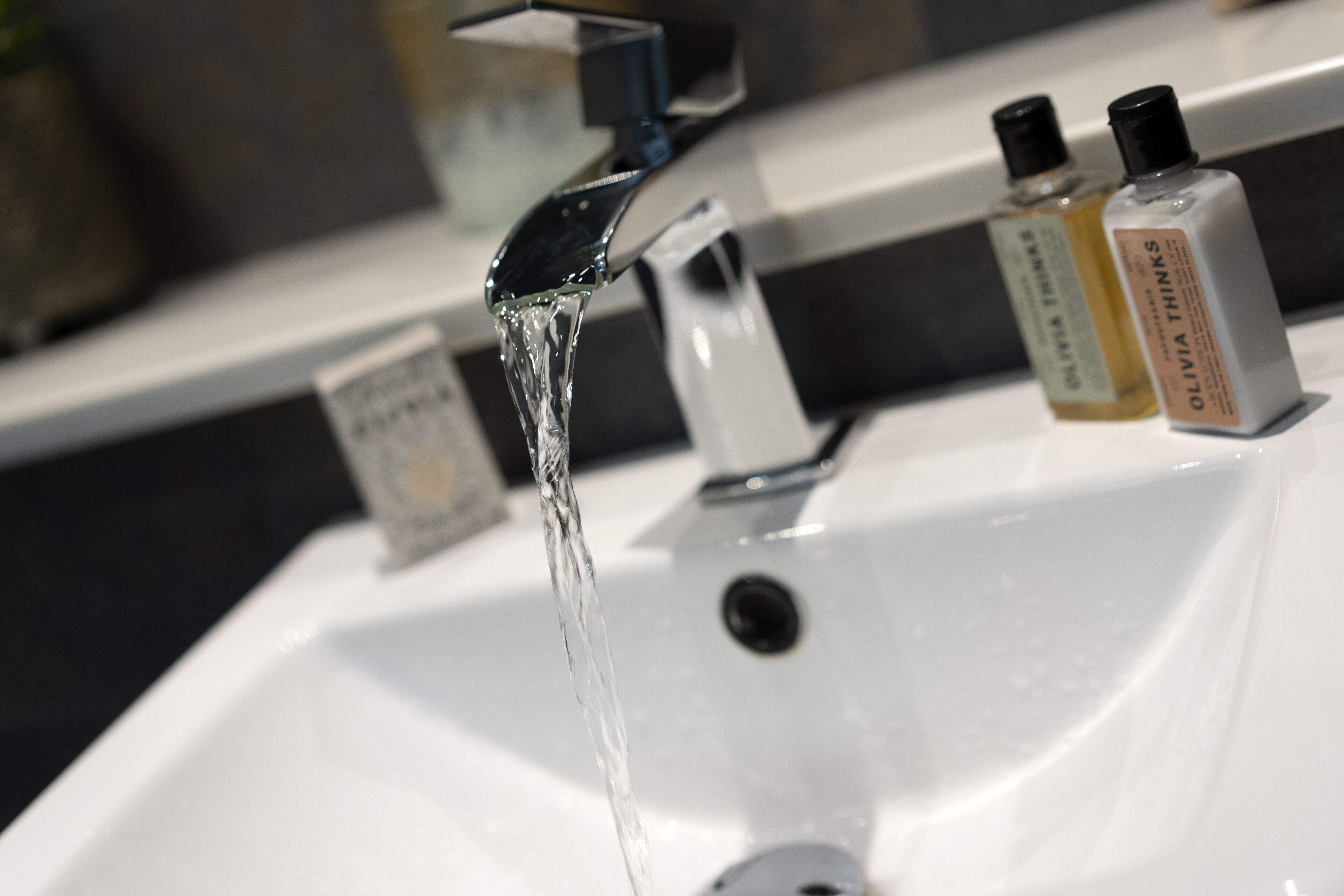 A bathroom sink with running water and two bottles of hand soap.