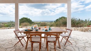 A wooden table set for breakfast with a scenic view of the sea and hills.