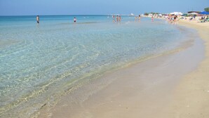 A beach with clear shallow waters, a sandy shore, and a few people in the distance.