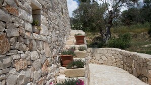 A stone staircase with terracotta pots containing flowers, leading up to a stone wall.