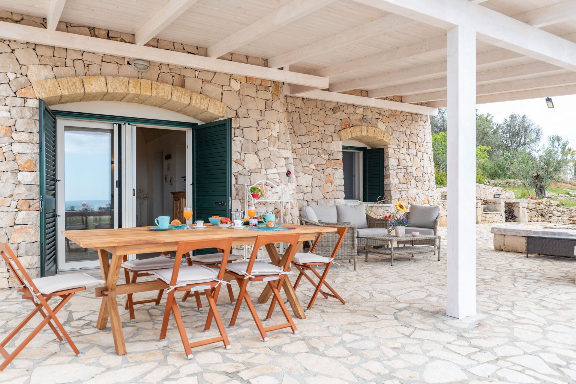 Un'area pranzo all'aperto coperta, con pareti in pietra, un tavolo e sedie in legno.