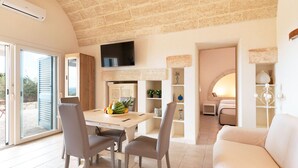 A spacious living area with a dining table, chairs, a sofa, and a TV mounted on the wall.