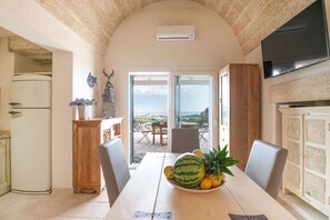 Un comedor con una mesa dispuesta para dos personas, un refrigerador y un televisor montado en la pared.