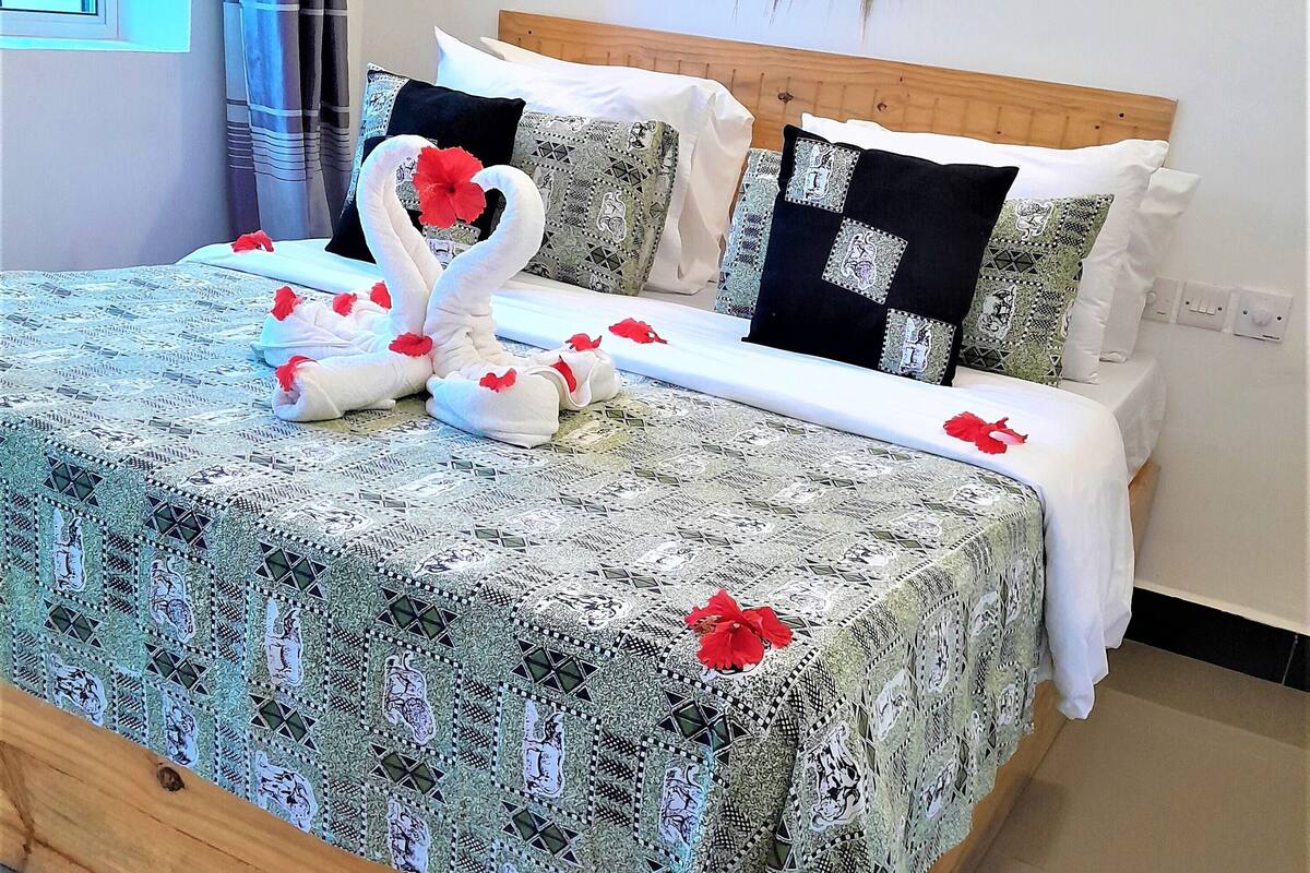 Una cama bien hecha con un edredón estampado, almohadas decorativas y una toalla dispuesta en forma de cisne.