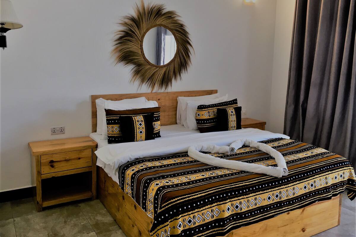 Una cama bien hecha con ropa de cama estampada, un cabecero de madera y una mesita de noche con una lámpara.