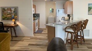 A modern kitchen with a central island, wooden cabinets, and a dining area with wicker chairs. - Beautiful 2/2 Villa w/4 Seater Gas Golf Cart, BBQ Grill, and WiFi!! (The Villages)