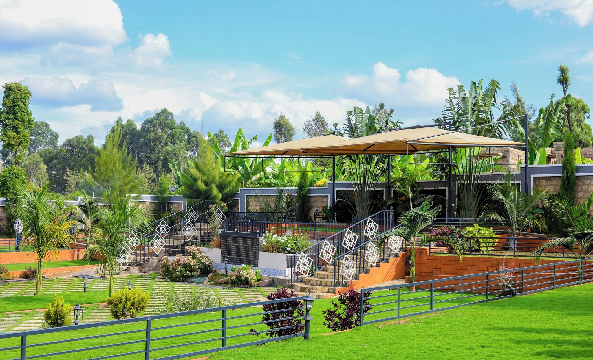 Hotel de diseño moderno, con un espacio exterior cubierto y escaleras que conducen a un edificio, rodeado de exuberante vegetación y palmeras.