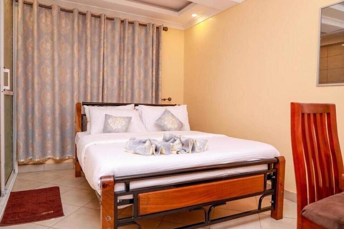 Una cama individual con estructura de madera, una mesita de noche, una silla y una ventana con cortinas.