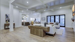 Een ruime woonkamer met een houten salontafel, een witte bank en een eethoek, met een keuken op de achtergrond.