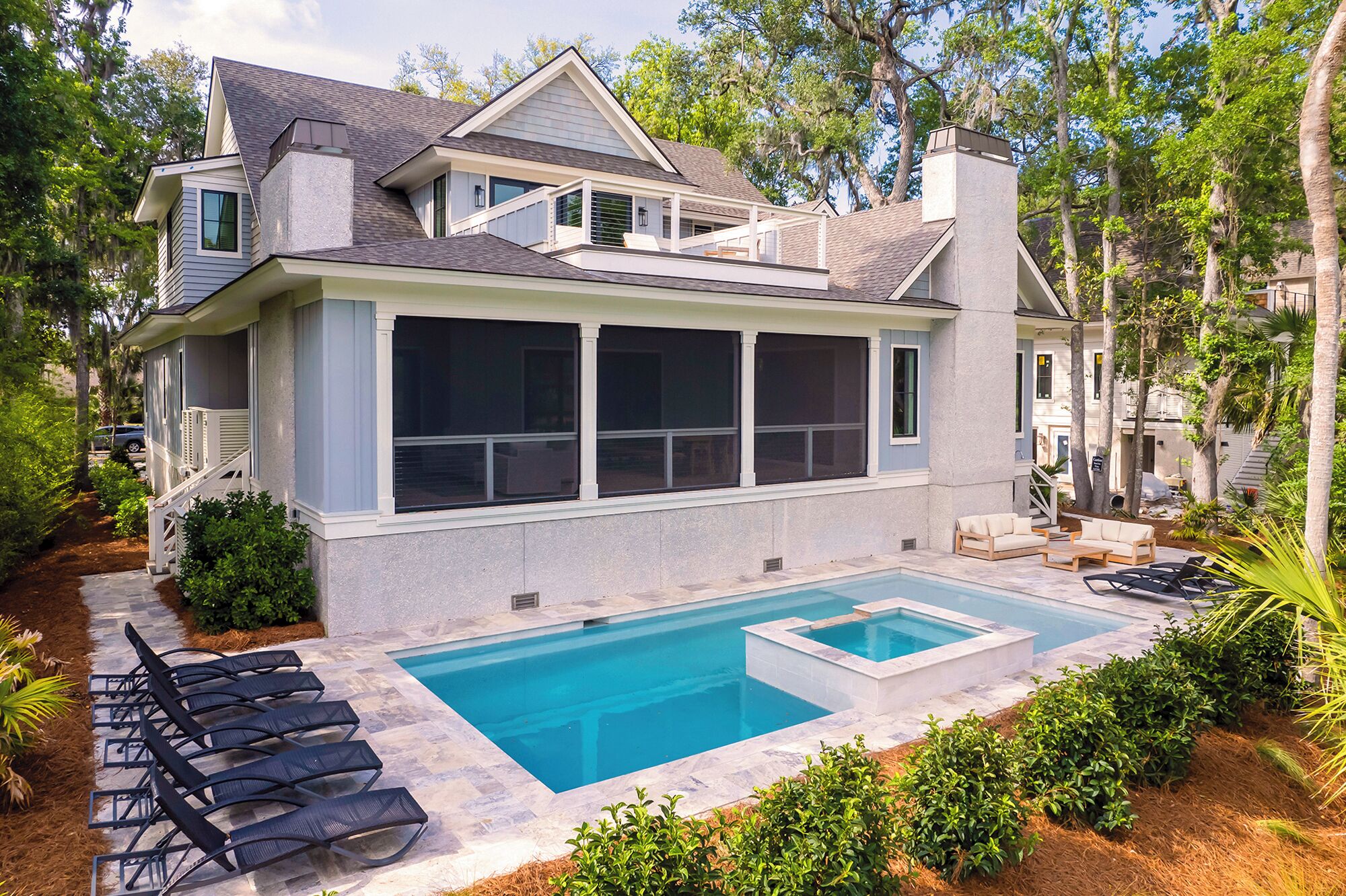 Uma casa moderna de dois andares com uma piscina grande e área de estar externa.