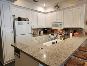 A kitchen with white cabinets, a granite countertop, a stainless steel refrigerator, a microwave, a stove, and a sink.