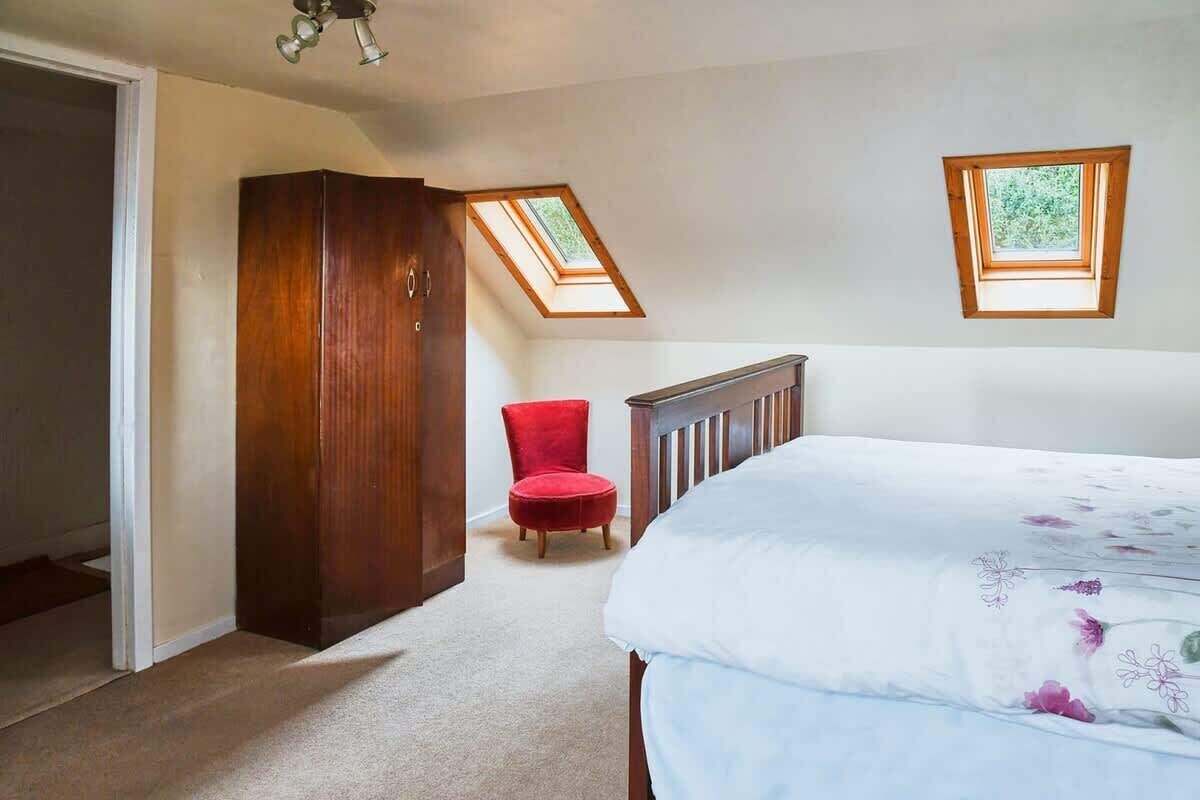 Une chambre à coucher avec un grand lit, un fauteuil rouge, une armoire et deux fenêtres de toit.