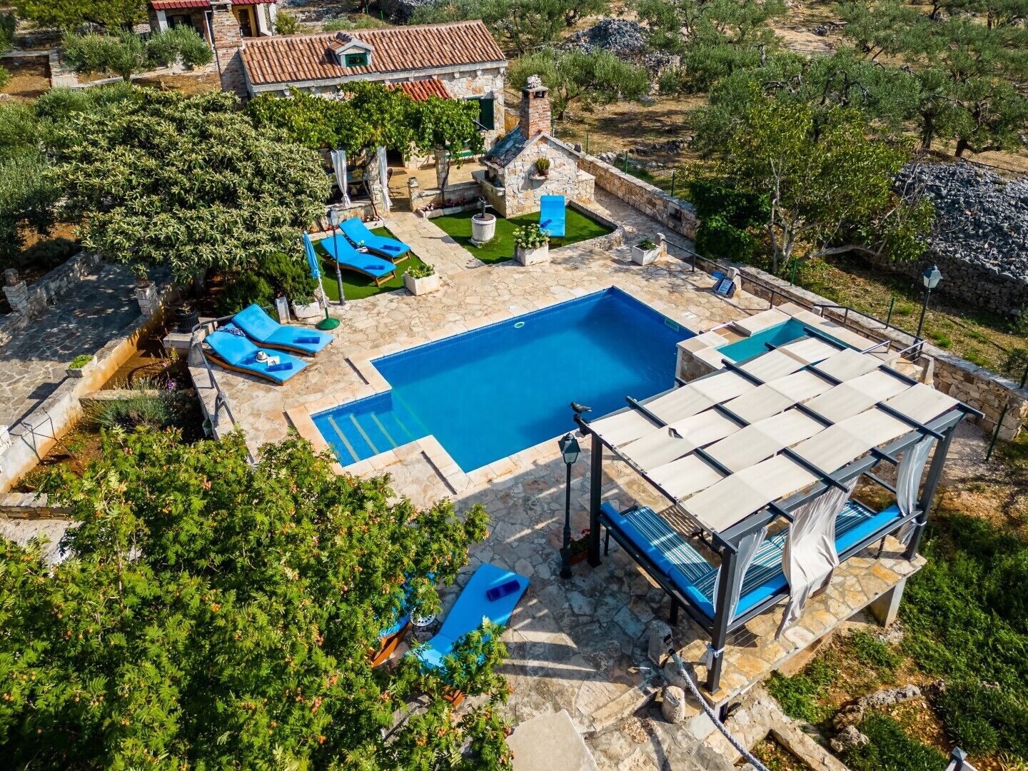 An aerial view of a property with a swimming pool, outdoor seating, and a stone building.